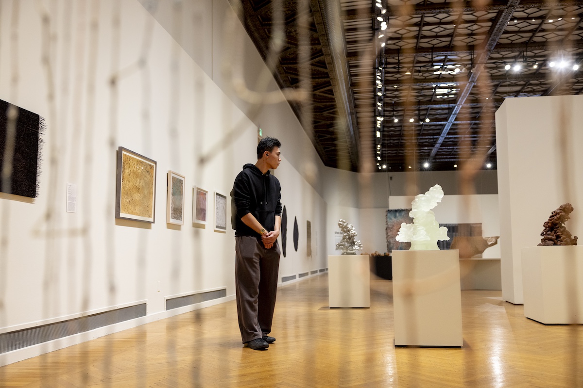 Man in cap contemplatively viewing sculptures in a warm-lit museum gallery