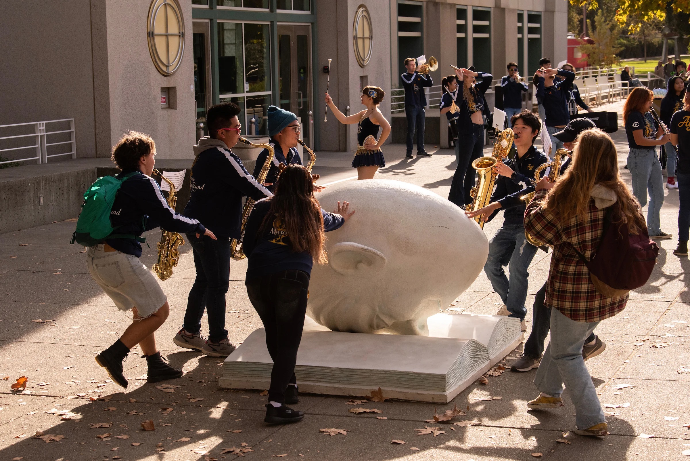 Members of the UC Davis marching band play their instruments and rub the Bookhead, a large sculpture of a head with its nose in a book, for good luck
