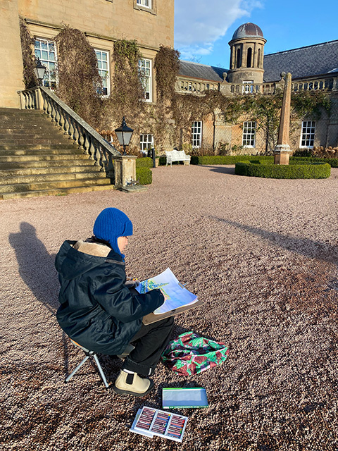 UC Davis alumna Layne Takahashi, wearing a blue winter hat, sits outside near buildings drawing from observation.
