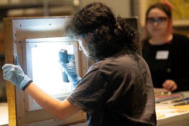 A person looks at a bright panel while another individual observes in the background.