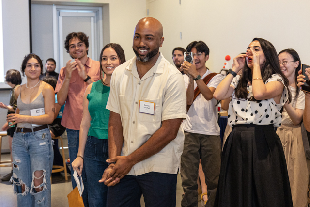 Damien Mitchell, who identifies as black, smiles while classmates, friends and colleagues stand behind him clapping, yelling and taking photos in support of him.