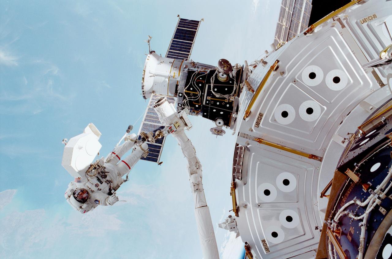 An astronaut attached to a robotic arm works outside the International Space Station. 