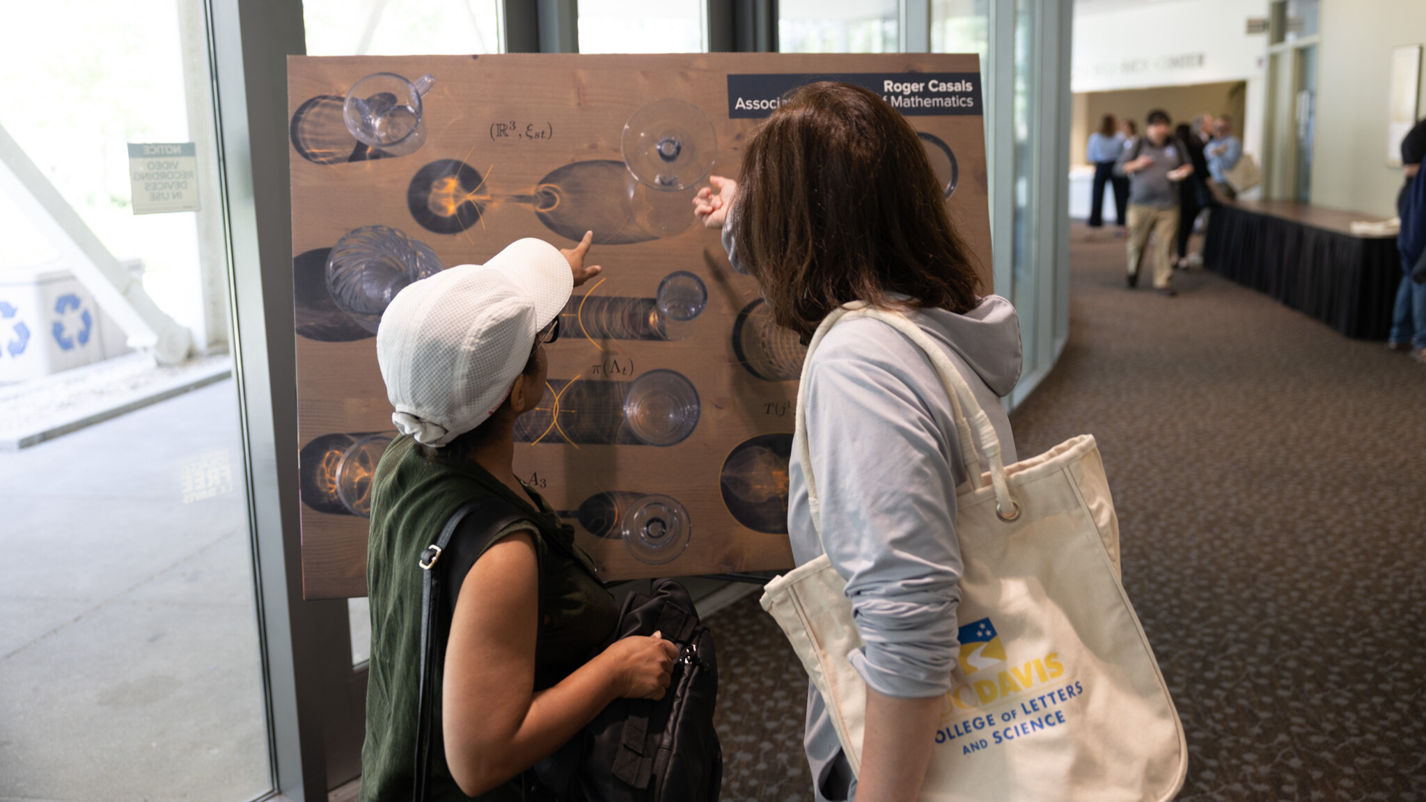Two people look at a poster showcasing light refracting through a variety of glasses. 