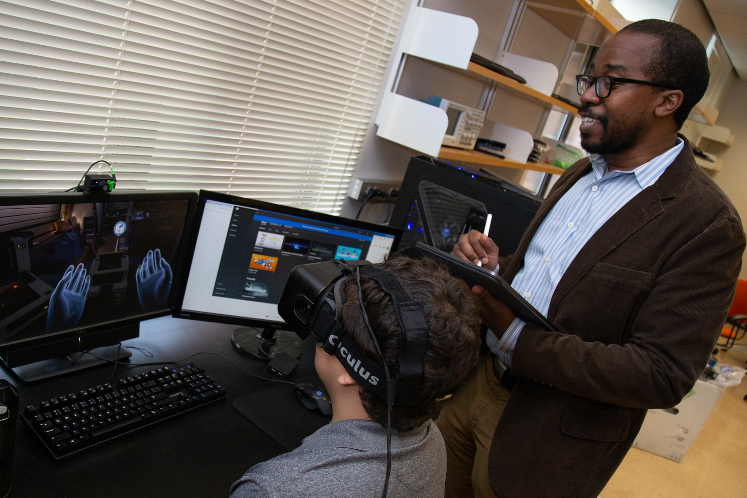 Wilsaan Joiner stands above a student who operates a computer with a virtual reality headset. 