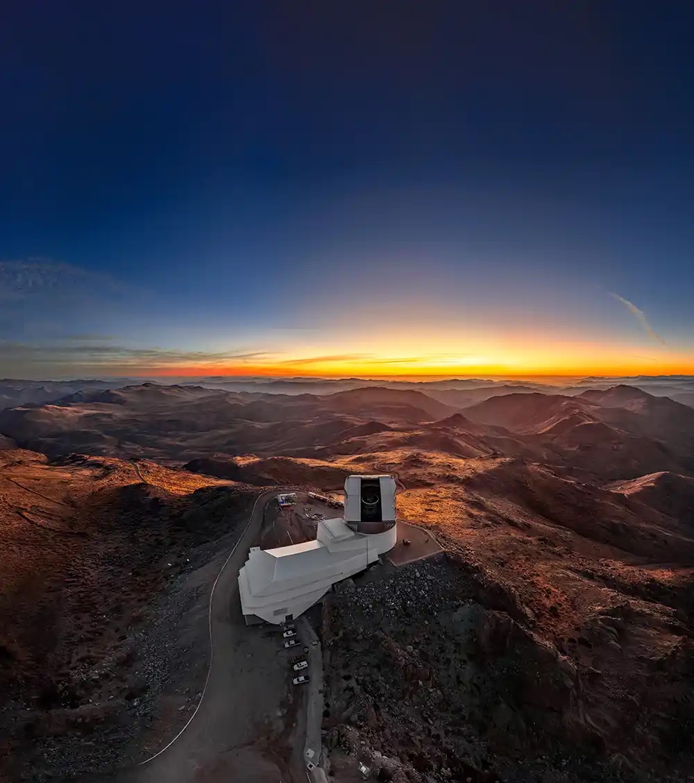 Mountaintop white observatory at sunset over rugged orange-lit hills
