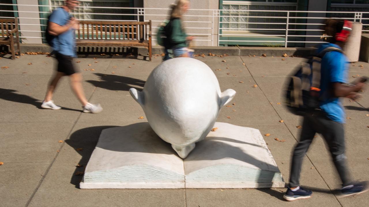 People pass by the Egghead 'Bookhead' sculpture, which features a head with its nose in a book