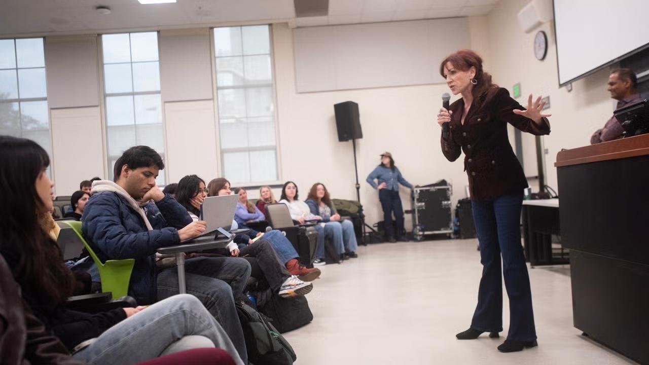 A speaker engaging with an audience in a lecture hall setting.