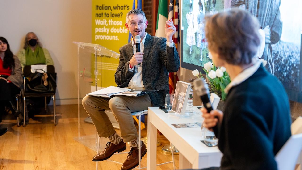 Two people conversing at a panel in a bright room, yellow poster behind