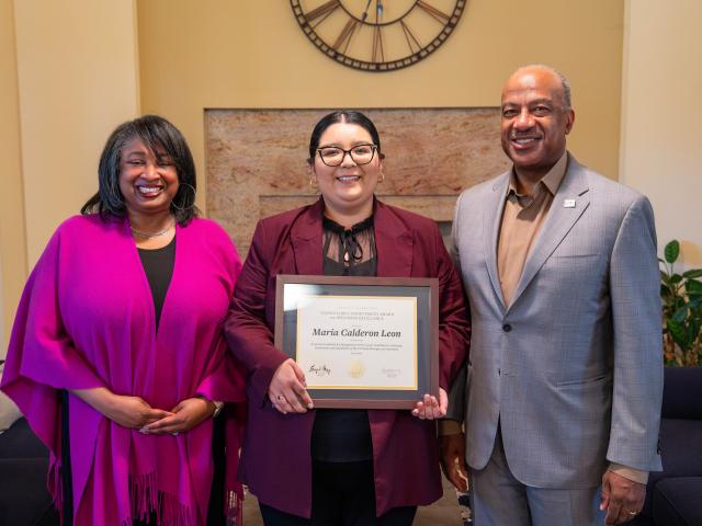 Three smiling professionals; center holds framed certificate, left in magenta, right in gray.