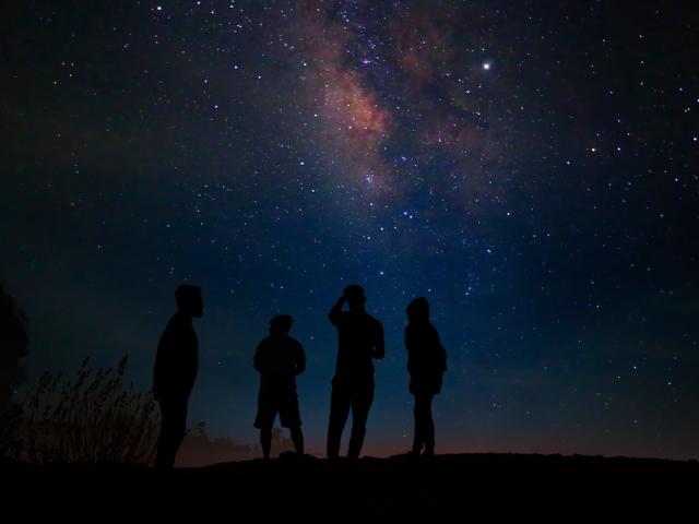 Four silhouetted people on a ridge gazing at the Milky Way under a starry sky