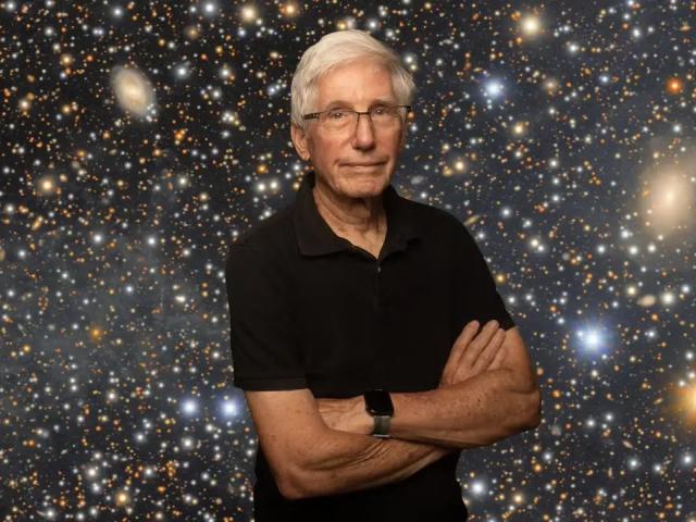 Older man with white hair and glasses, arms crossed, against star-filled galaxy backdrop