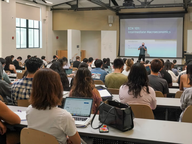 University lecture hall photograph with students facing presenter and projection screen