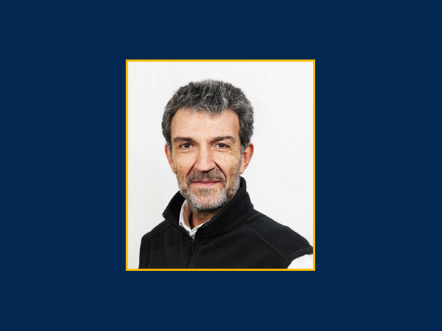 Headshot of smiling middle-aged man with salt-and-pepper beard on navy background