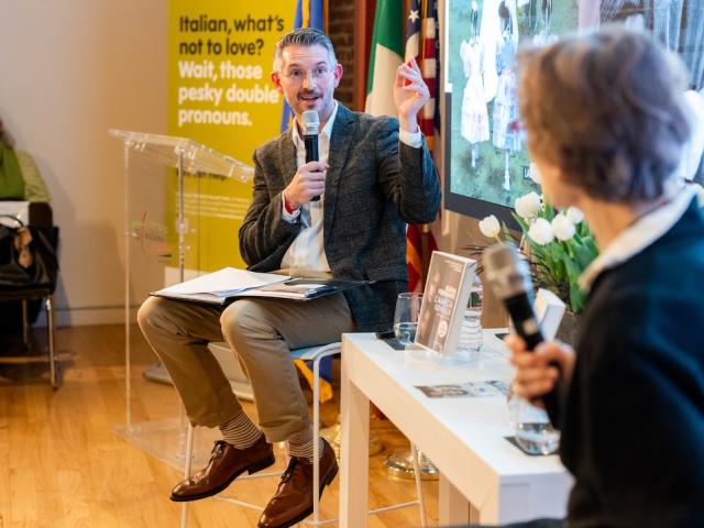 Two people conversing at a panel in a bright room, yellow poster behind