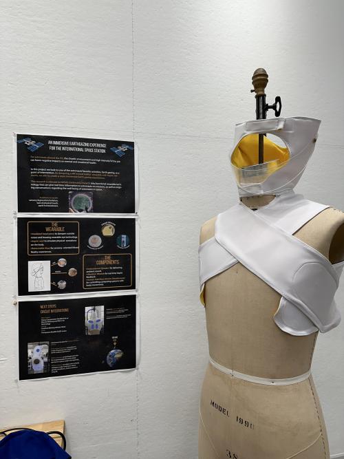 A poster is displayed next to a mannequin that wears a wearable prototype, which consists of a head piece, a visor and a vest. 
