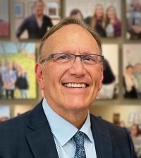Smiling man in a suit with glasses, surrounded by a collage of family photos.