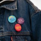 A close-up image of three pins/buttons -- blue, purple and red -- featuring the 'Eggheads' attached to a denim jacket