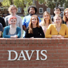 A group fo students stands behind a brick wall with UC Davis written on it