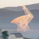 A radio telescope is shrouded in mist and surrounded by mountains. 