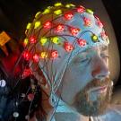 A man sits with a cap of electrodes on top of his head 