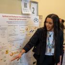 A student points to a poster as a bystander listens to her talk about research