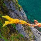 Two women in yellow (left) and orange (right) dangle off a cliff during a vertical dance performance.
