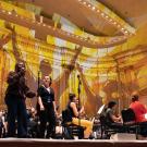 Orchestra and choir performing on stage under warm golden lighting in a concert hall