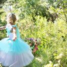 A young girl is wearing a blue dress and is playing in a green meadow 